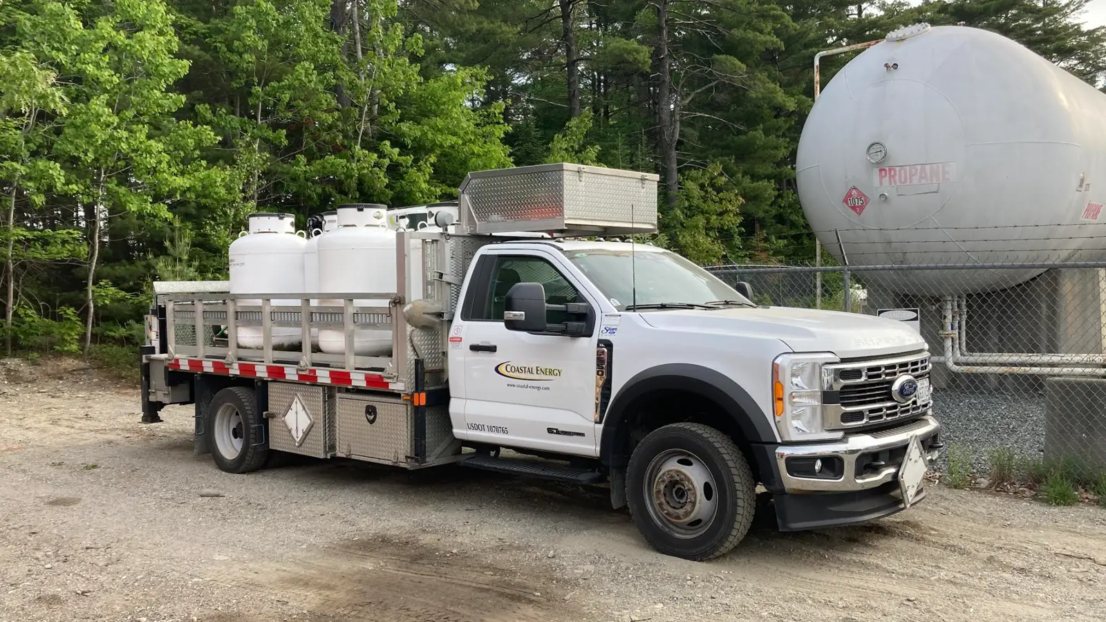 A white Coastal Energy Ford F-550 Super Duty Powerstroke diesel truck equipped with a flatbed, mini-crane, and propane tanks in the Mount Desert Island region.