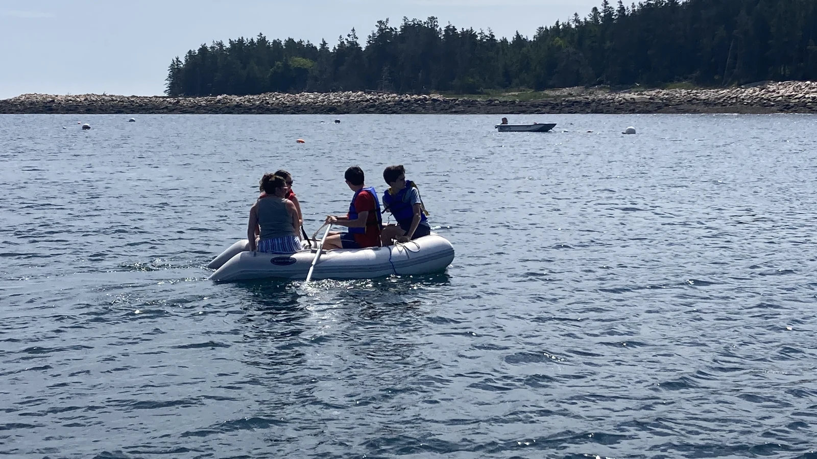 Family rowing an inflatable dinghy toward the rocky shore of Baker Island, Maine