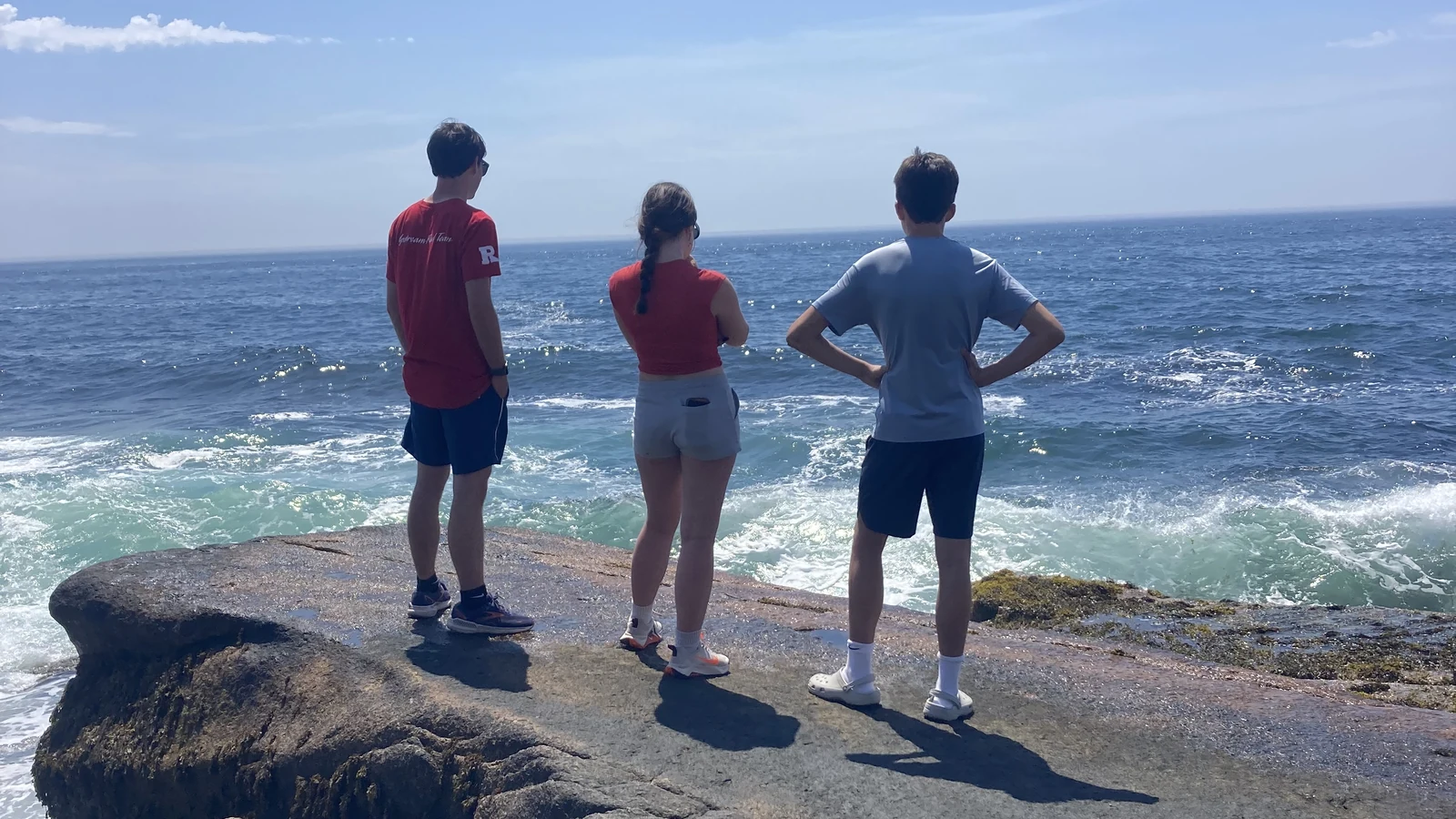 Three people walking along a rocky granite shoreline with breaking waves in coastal Maine