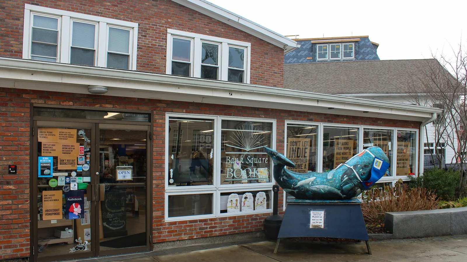 Brick exterior of Bank Square Books in Mystic, Connecticut, with a painted whale sculpture out front.