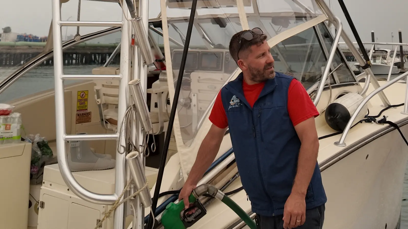 Peter Rauscher holding a fuel nozzle while fueling a sportfishing boat at a marina fuel dock, with an American flag flying from the boat's tower