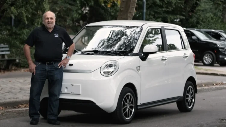 Wink Motors founder and CEO Mark Dweck standing beside a white Wink Mark III low-speed electric vehicle parked on a tree-lined street
