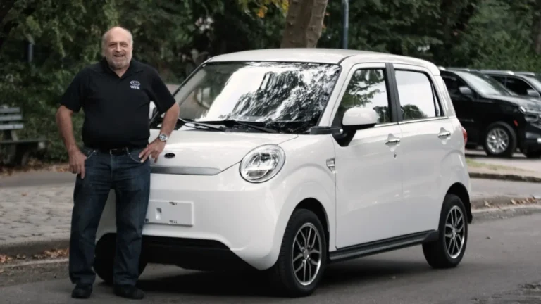 Wink Motors founder and CEO Mark Dweck standing beside a white Wink Mark III low-speed electric vehicle parked on a tree-lined street