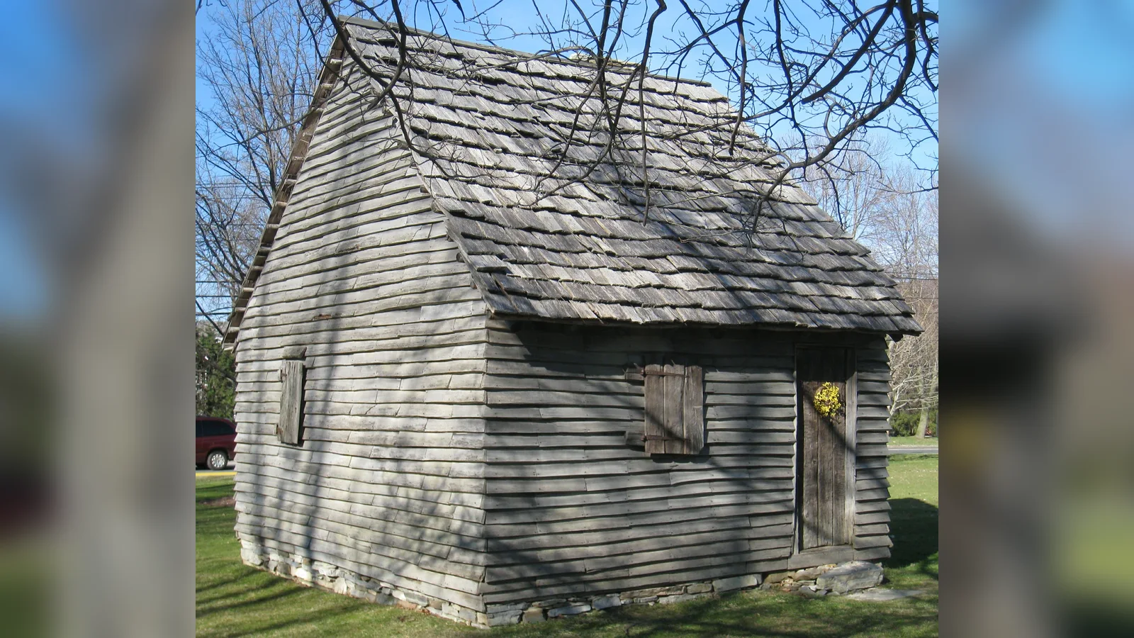 Replica colonial settler's hut with weathered gray wooden shingles and clapboards, known as the 1753 House, on a green in Williamstown, Massachusetts