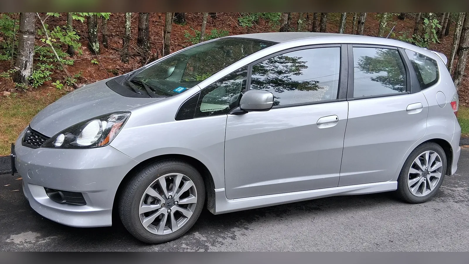 Front three-quarter view of a silver 2013 Honda Fit hatchback parked on a rural road