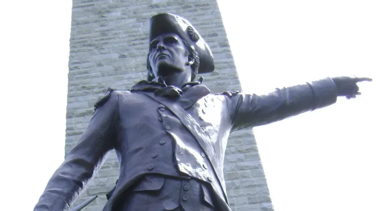 Bronze statue of General John Stark pointing forward, with the stone obelisk of the Bennington Battle Monument rising behind him in Bennington, Vermont