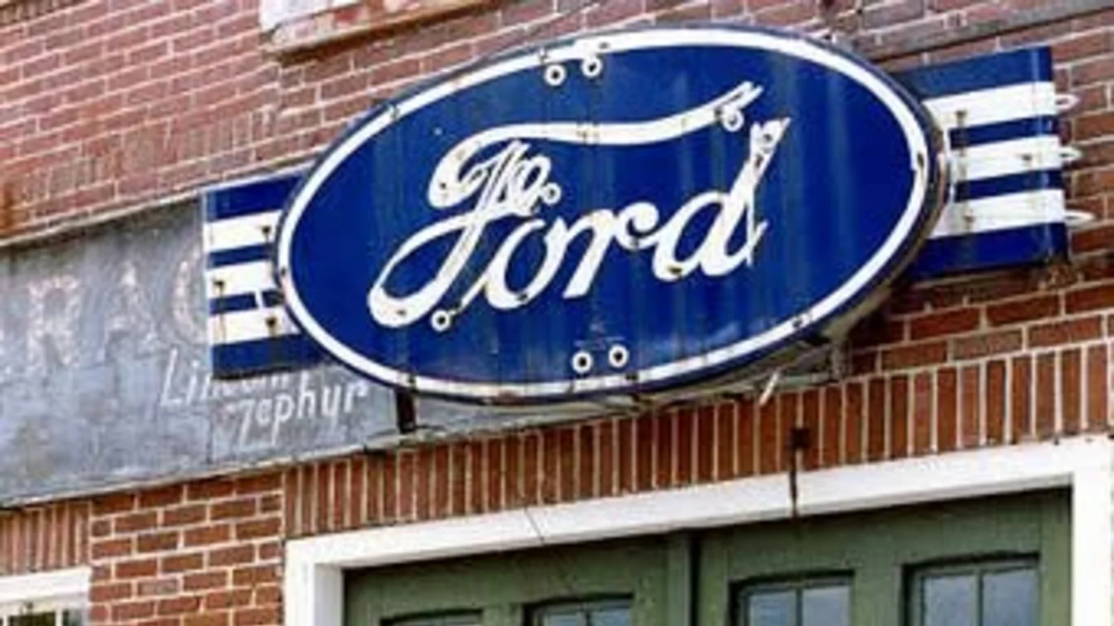 Blue oval Ford sign mounted on a brick wall above weathered green wooden garage doors at the former South Weare Garage in Weare, New Hampshire