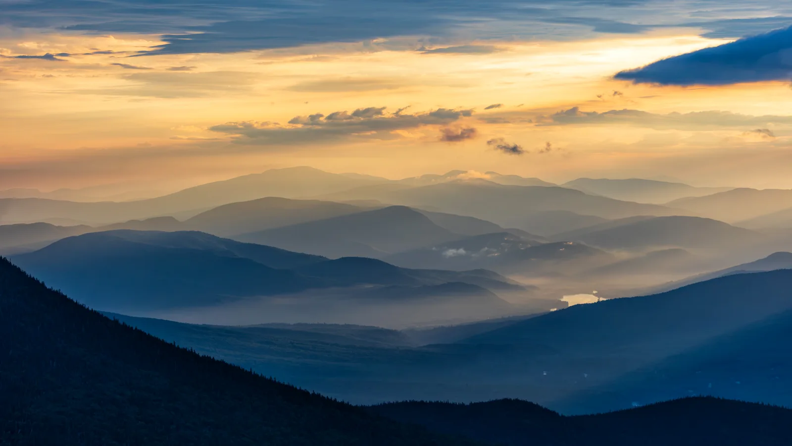 Layers of blue mountain ridges under an orange and gold sunrise sky, photographed from Mount Washington in New Hampshire.