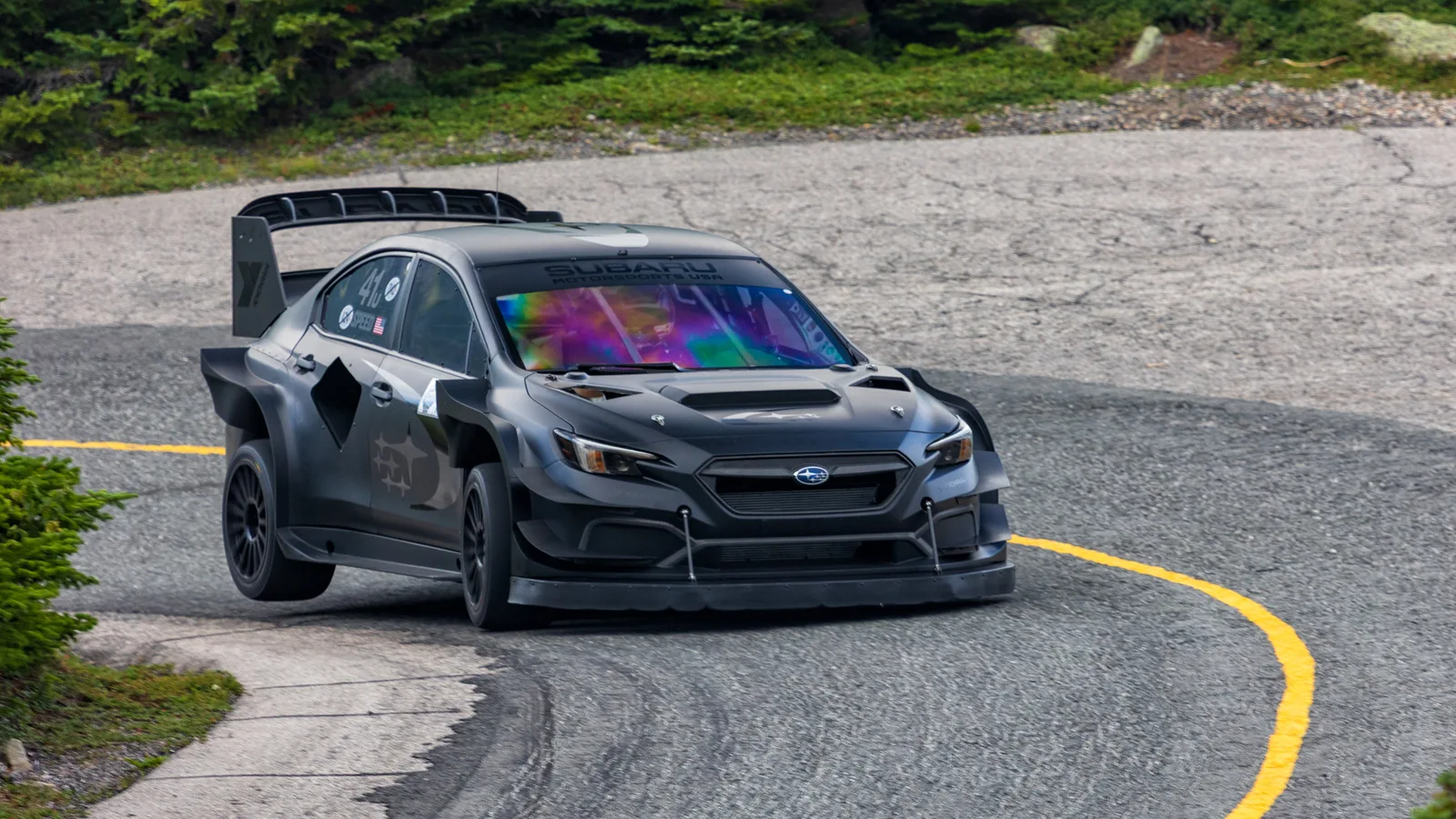 Matte black Project Midnight Subaru WRX hillclimb car with a large rear wing cornering on the paved Mount Washington Auto Road.