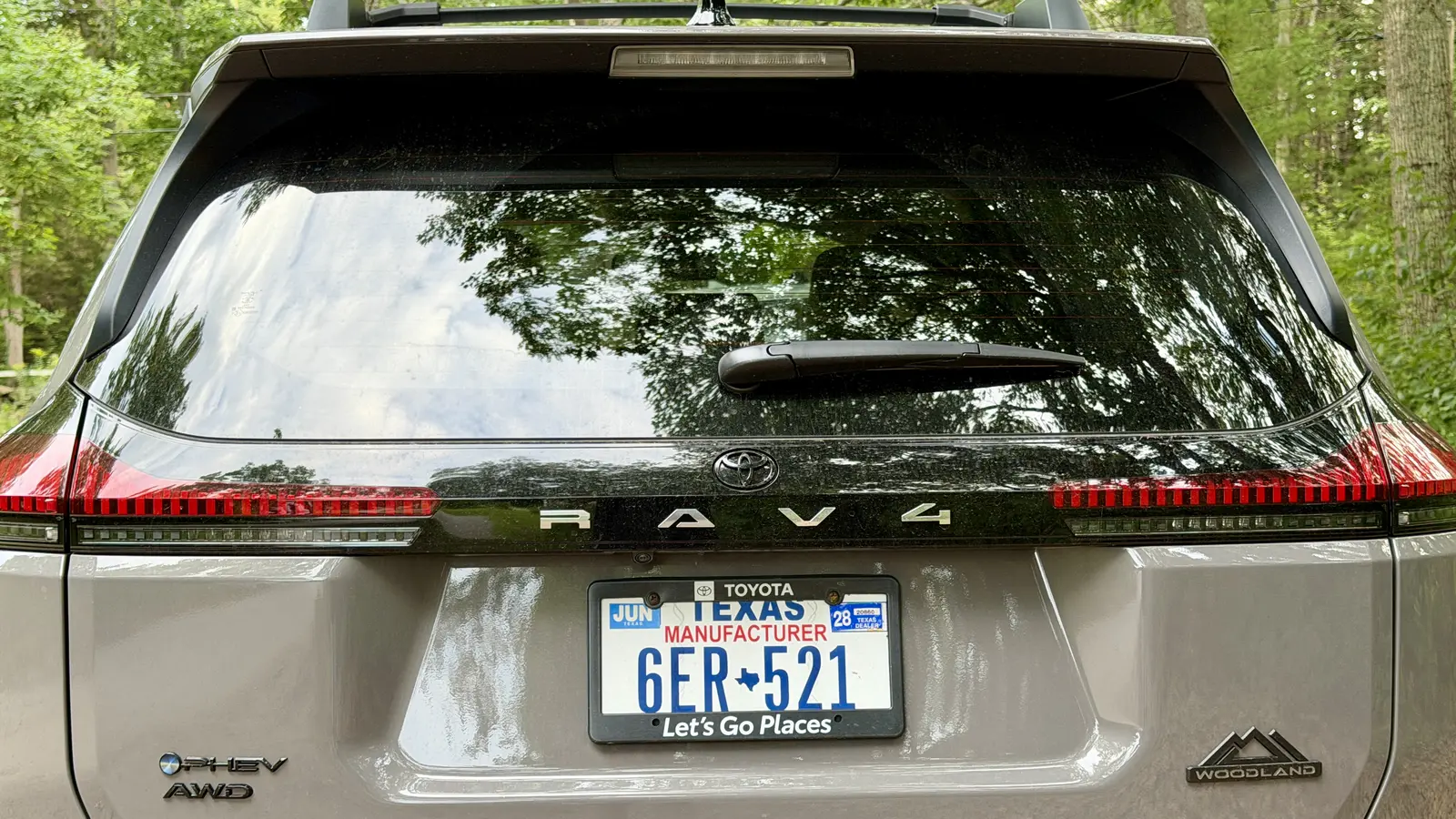 Rear hatch of a gray 2026 Toyota RAV4 with PHEV AWD and Woodland badges and full-width taillights