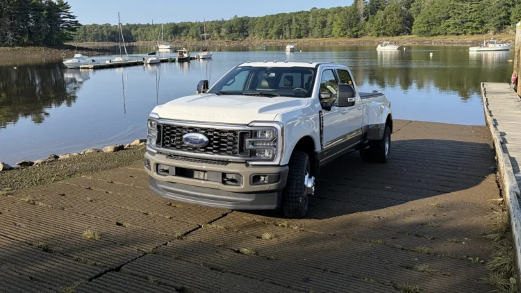White Ford F-350 Super Duty crew cab dually pickup truck parked on a boat ramp at a Maine harbor with moored boats behind it
