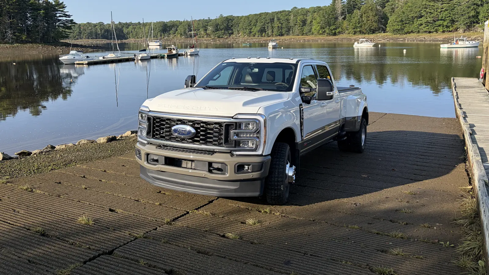 White Ford F-350 Super Duty crew cab dually pickup truck parked on a boat ramp at a Maine harbor with moored boats behind it