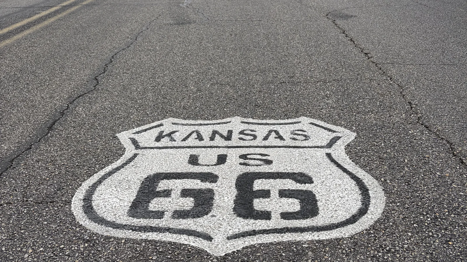 A white Kansas US 66 highway shield painted on the asphalt of Route 66 in Galena, Kansas.