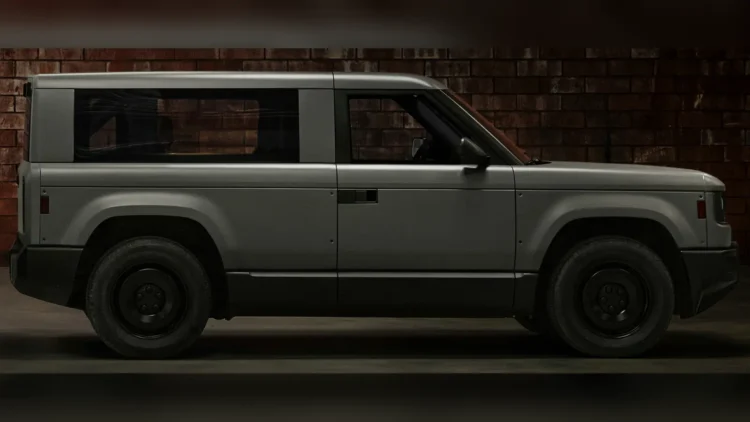 Matte gray Slate electric truck fitted with an enclosed SUV body kit, seen in side profile against a dark brick wall.