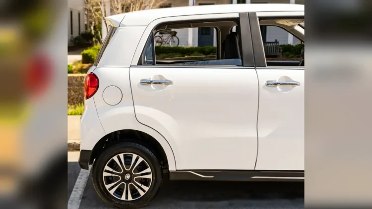Rear passenger door, taillight, and rear wheel of a white Wink Mark3 electric microcar parked on a street.